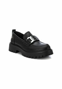 Zapatos de cuero negro tipo slip-on con suela de goma gruesa, que cuentan con un acento de hebilla plateada y un detalle texturizado a lo largo del perímetro.