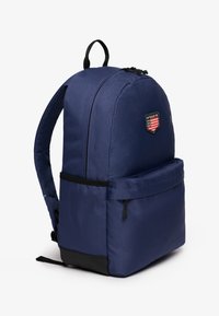 Mochila azul marino hecha de un tejido duradero, con un bolsillo frontal, cremalleras y un parche con un diseño de la bandera estadounidense.