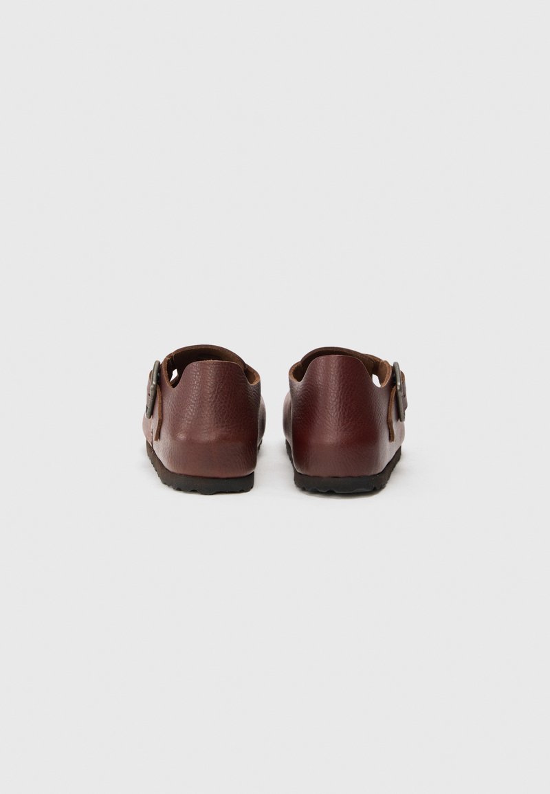 Zapatos de cuero marrón con forma redondeada, que presentan un cierre lateral y un diseño de talón abierto, superficie texturizada y suela de goma con relieve.