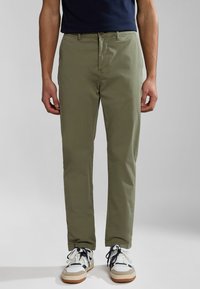 Chinos de color verde oliva claro con un corte recto, material de algodón, cierre de botón, bolsillos laterales y líneas limpias combinados con zapatillas blancas y beige.