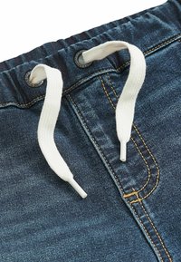 Pantalon en denim bleu foncé à taille élastique avec cordon de serrage en tissu blanc passant à travers des œillets métalliques.