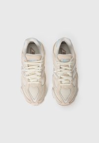 Une paire de chaussures de course New Balance beige et blanche avec des détails en maille et en daim, vue de dessus sur un fond blanc.