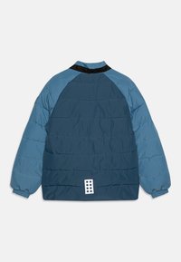 Jachetă căptușită cu un design color-block, având secțiuni în albastru marin și albastru deschis, guler negru și accente albe la nasturi pe spate.