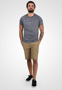 Kortærmet, grå tekstureret t-shirt, parret med beige knælange shorts og sorte sneakers, med et enkelt design med lommer.