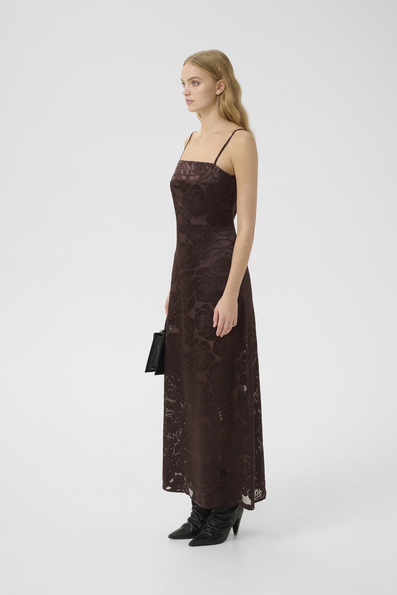Robe longue à motif floral brun foncé avec des bretelles fines, texture légère, associée à des bottes à talons hauts noires et à un sac.