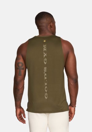 Muscular man with arm tattoos wearing an olive green sleeveless gym shirt with "Gold's Gym" text on the back, standing against a plain background.