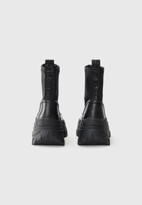 Czarne botki za kostkę o smukłym designie, gładkie skórzane i materiałowe wykończenia, teksturowane, masywne podeszwy oraz wyraźne czarne oznaczenia na obcasach.