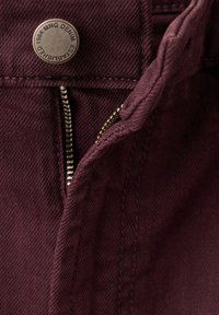 Jeansy dżinsowe w kolorze bordo z częściowo odsłoniętym mosiężnym zamkiem błyskawicznym i metalowym guzikiem z napisem "MNG DENIM ESTABLISHED 1984."