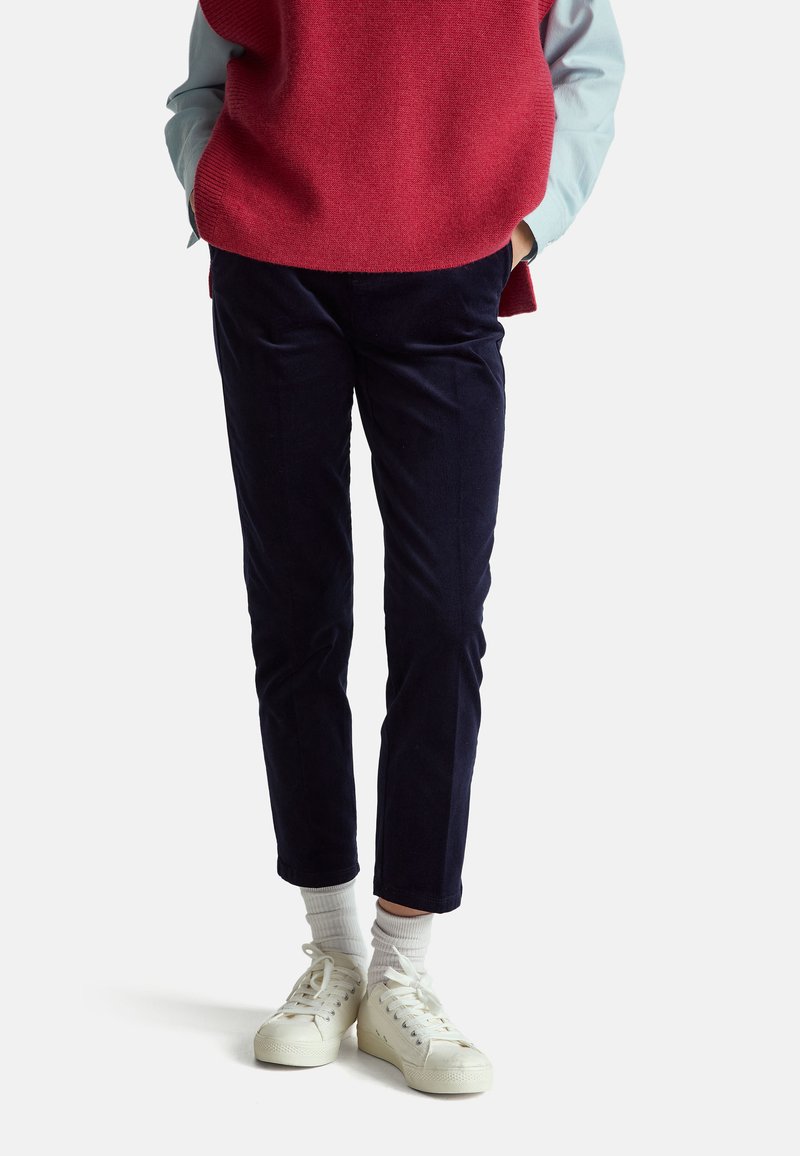 Navy corduroy trousers with a slim fit, paired with a red sweater and white sneakers, showcasing ribbed texture and subtle tailoring details.