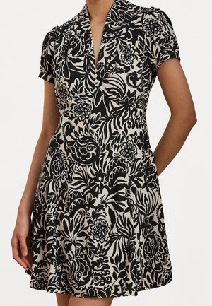 Femme portant une robe à manches courtes avec un motif floral noir et blanc, des boutons sur le devant et un col en V.