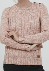 Maglione a coste in morbido pesco con un motivo testurizzato, scollatura rotonda e due bottoni marroni sulla spalla. Presenta polsini a costine.