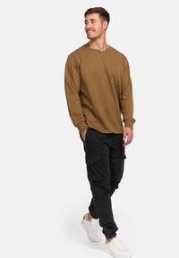 Brun långärmad skjorta med ficka, kombinerad med svarta cargobyxor med flera fickor, och vita sneakers.
