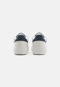 Sneaker in pelle bianca e blu navy con texture liscia, caratterizzati da una suola spessa bianca e un logo impresso sul tallone.