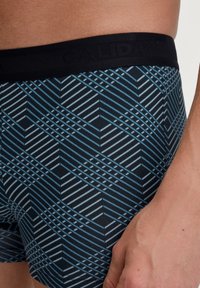 Zwarte boxershorts met een blauw en wit gestreept geometrisch patroon. Zachte stof met een zwarte elastische tailleband met het "CALIDA" logo.