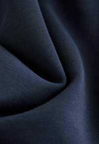 Dunkelblauer Stoff mit dicht gestrickter Textur, gefaltet, um sanfte, geschwungene Schatten und Highlights zu erzeugen, die seine glatte Oberfläche betonen.