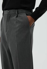 Grijze op maat gemaakte broek van een getextureerde stof, voorzien van zijzakken, een platte voorkant en twee knoopsluitingen aan de tailleband.