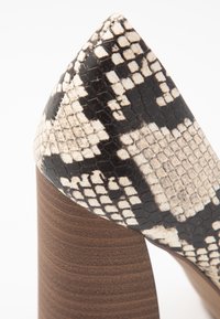 Escarpin à bout pointu en motif serpent noir et blanc avec surface texturée ; talon en bois empilé présentant des rainures horizontales.