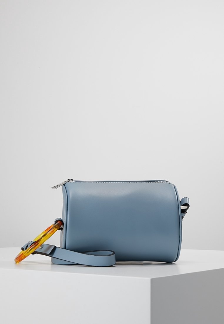 Borsa in finta pelle blu chiaro con chiusura a zip, tracolla regolabile e manico trasparente multicolore. Texture liscia con un design minimale.