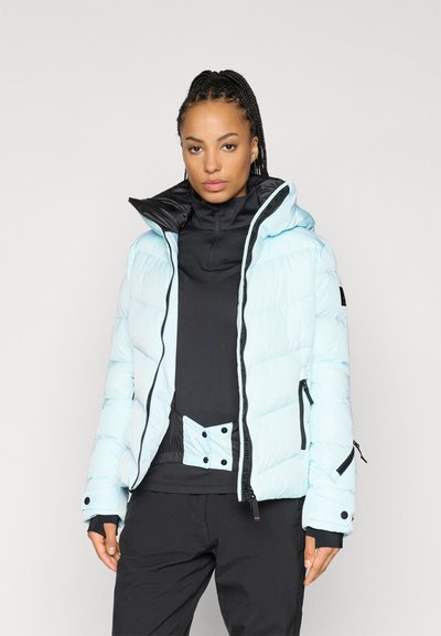 Ανοιχτό μπλε φούτερ μπουφάν με μαύρο κλείσιμο στον γιακά, μπροστινές τσέπες και κομψό σχέδιο, φορεμένο πάνω από μια μαύρη μπλούζα.