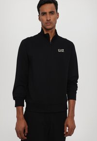 Sort zip-up sweatshirt i blød stof med ribstrikkede manchetter og kant, med et lille guldlogo på brystet.