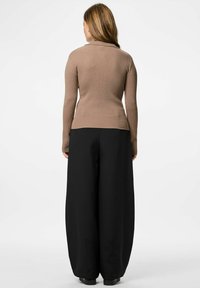 Suéter marrón de cuello alto acanalado con mangas largas, combinado con pantalones amplios negros de pierna ancha, visible desde la parte de atrás.
