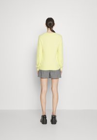 Żółty, miękki sweter z prążkowanymi mankietami, zestawiony z czarno-białymi kratkowymi szortami. Model nosi masywne czarne buty na platformie.