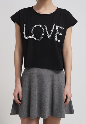 T-shirt court noir avec "LOVE" écrit en points floraux blancs, assorti à une jupe grise taille haute de coupe trapèze portée par une personne debout.