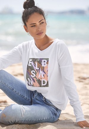 White long-sleeve shirt featuring a colorful graphic with letters on a green background; paired with light blue distressed jeans.