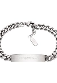 Pulsera de cadena de metal plateada con una placa plana grabada con "EMPORIO ARMANI" y una pequeña etiqueta con un logo adjunta.