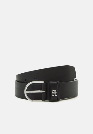 Zwarte leren riem met zilverkleurige afgeronde gesp en gestikte lus met zilverkleurig metalen "TH" logo op een effen lichte achtergrond.