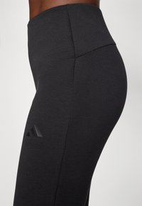 Ψηλόμεσες μαύρες κολάν από λείο ύφασμα, με μινιμαλιστικό σχέδιο και ανάγλυφο μαύρο λογότυπο στην αριστερή πλευρά.