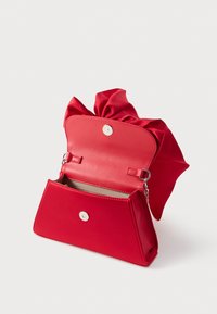 Punainen käsilaukku, jossa magneettikiinnitys, avoin läppä paljastaa beigen vuorin ja pehmeän kangasdetailin yläosassa.