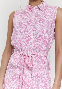 Abito senza maniche in tessuto leggero con un motivo floreale rosa su sfondo bianco, con dettaglio in vita annodato e colletto.
