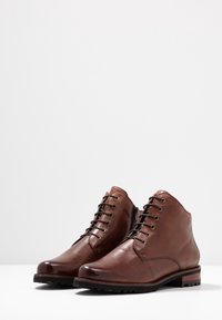 Bottines en cuir marron avec bouts ronds, design à lacets et surface texturée. Équipées d'œillets en métal et d'une semelle noire robuste.