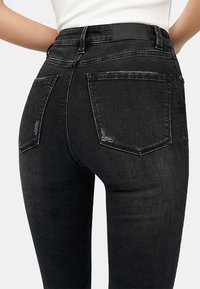 Jeans de mezclilla negros con un diseño ajustado, que cuentan con bolsillos traseros, un ligero desgaste y una etiqueta en la cinturilla sencilla. Textura suave, forma esbelta.