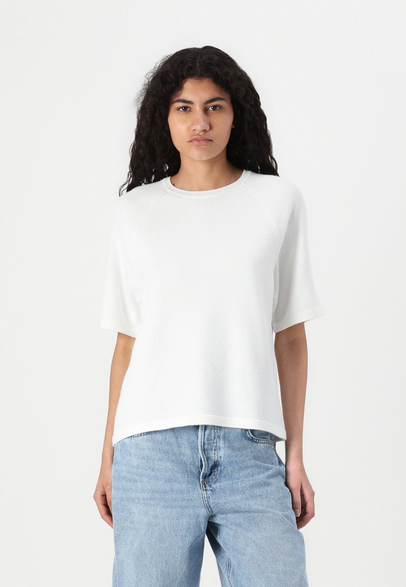 Maglietta a maniche corte bianca in maglia con scollo rotondo, caratterizzata da una vestibilità comoda e una texture delicata, abbinata a jeans di denim blu chiaro.