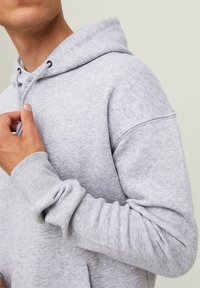 Felpa grigia realizzata in tessuto morbido, dotata di cappuccio con lacci, polsini a costine e una vestibilità comoda. Design semplice senza motivi o loghi.