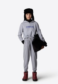 Felpa grigia con il logo "THE NORTH FACE", pantaloni della tuta grigi, stivali da neve rossi e un cappello di pelliccia nera. L'outfit ha un aspetto casual e stratificato.