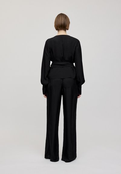 Zwarte outfit met een langslavige top met een tailleband en wijdvallende broek, beide gemaakt van een gladde, elegante stof.