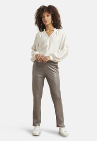 White long-sleeve blouse with a collar and textured sleeves, paired with sleek, light gray pants. Model wears white sneakers.
