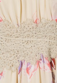 Cream floral patterned fabric with a beige lace trim. Focus on intricate lace detailing against soft, flowing material.