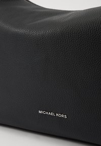Black leather handbag with a textured finish, featuring a silver "MICHAEL KORS" logo on the front for detail.