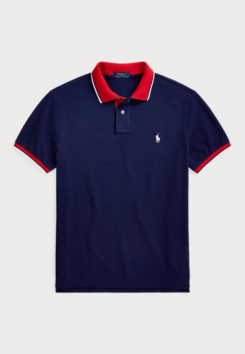 Polo shirt marine avec col rouge et accents de manches, arborant un logo blanc sur la poitrine gauche et une placket à deux boutons. Matière en coton.