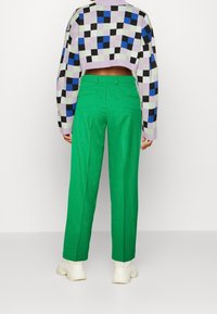 Cropped sweater in purple, black, and green checker pattern, paired with high-waisted, straight-leg green trousers and white sneakers.