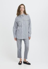 Gestreiftes Hemd in Blau und Weiß, mit zwei Brusttaschen, lockere Passform, kombiniert mit hellgrauen, geraden Jeans und schwarzen Ballerinas.