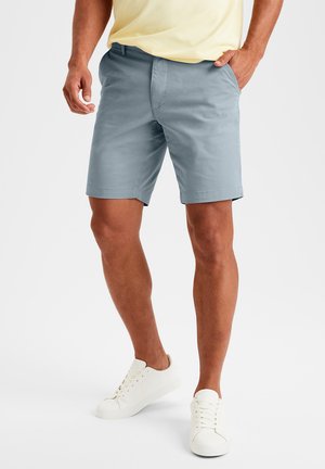 Helle blaue Baumwollshorts für Herren mit geradem Schnitt, zwei Vordertaschen und flachem Design, kombiniert mit weißen Sneakern.