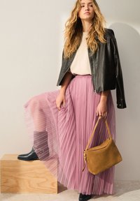 Jupe longue plissée rose clair associée à un haut crème et une veste en cuir noire. Bottines noires et sac à main en daim beige complètent la tenue.