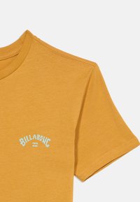 Κίτρινο T-shirt με κοντά μανίκια σε μουστάρδι απόχρωση, με μικρό λευκό λογότυπο "Billabong" τυπωμένο στο στήθος.