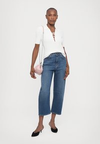 Hvid ribbet strikket polo shirt med snørebånd i halsen, parret med højtaljede blå denim brede bukser. Accessoriseret med en lille lyserød håndtaske.