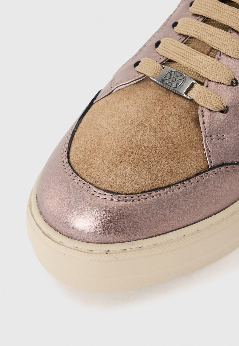Deportiva con una parte superior de cuero metálico color rosa dorado, puntera de ante color marrón claro, cordones beige y suela de goma color crema. Detalle de costura sutil presente.